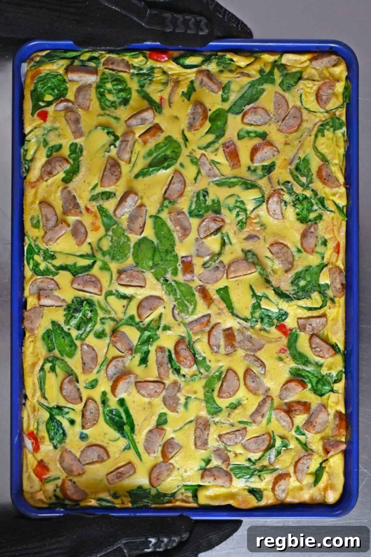 An overhead shot of freshly baked sheet pan eggs with sliced chicken apple sausage, baby spinach, red onions, and bell peppers.