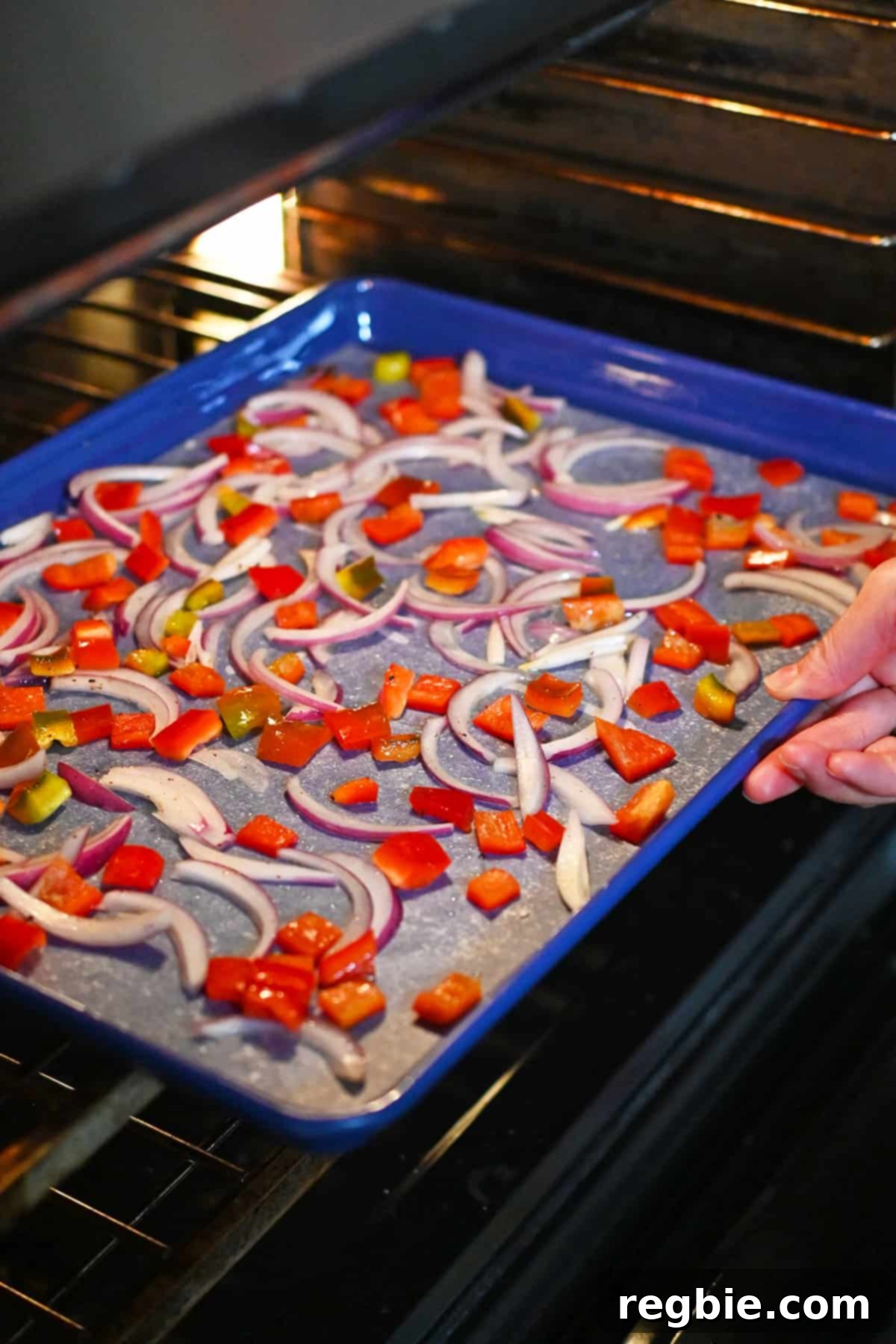 Putting a rimmed sheet pan with thinly sliced red onions and diced bell peppers into an open oven.