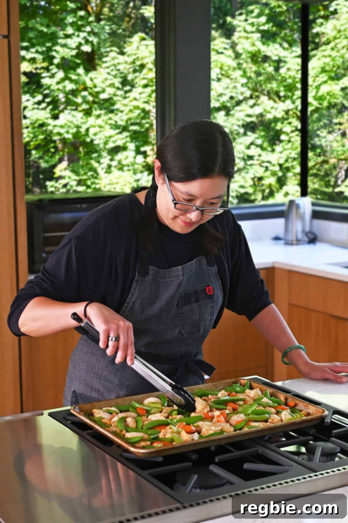Sheet Pan Cashew Chicken: Paleo & Whole30 Perfection 17 An Asian woman expertly using a pair of tongs to toss the freshly cooked Sheet Pan Cashew Chicken, ensuring every piece is coated in sauce before serving.