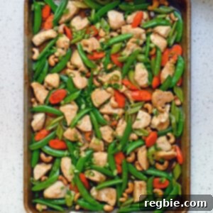 An overhead view of two hands holding a pan of Sheet Pan Cashew Chicken, ready to be served from the sheet pan.