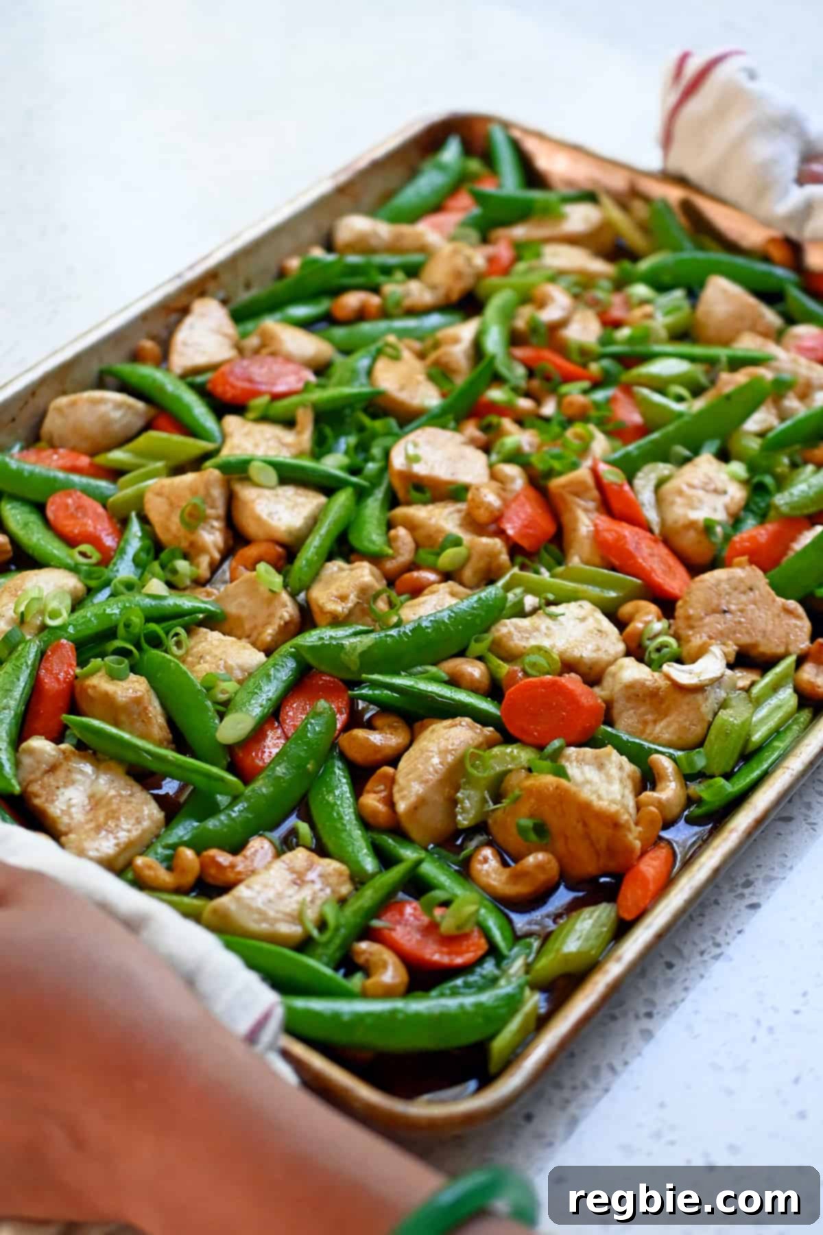 Sheet Pan Cashew Chicken: Paleo & Whole30 Perfection 3 A side view of two hands holding a sheet pan of freshly baked cashew chicken, steaming hot and straight out of the oven.