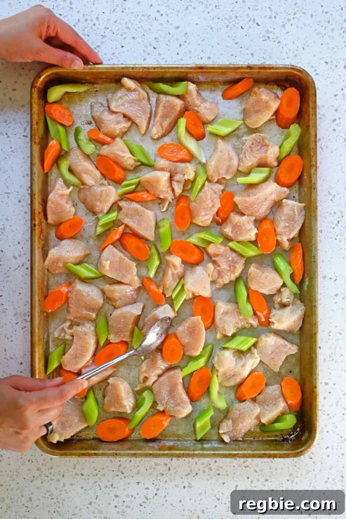 Sheet Pan Cashew Chicken: Paleo & Whole30 Perfection 9 A spoon meticulously arranging raw chicken breast pieces, sliced carrots, and sliced celery into a perfectly even single layer on a rimmed sheet pan.
