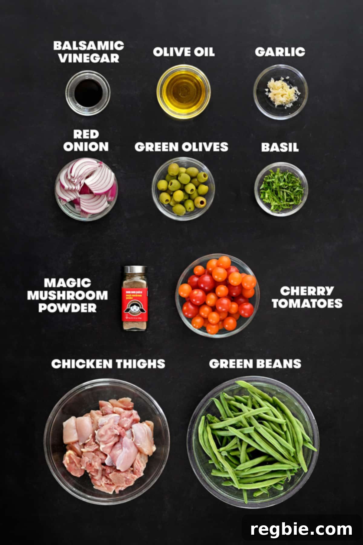 An overhead shot of the labelled and prepped raw ingredients to make sheet pan Italian chicken, including chicken, green beans, tomatoes, olives, onion, garlic, olive oil, and seasoning.