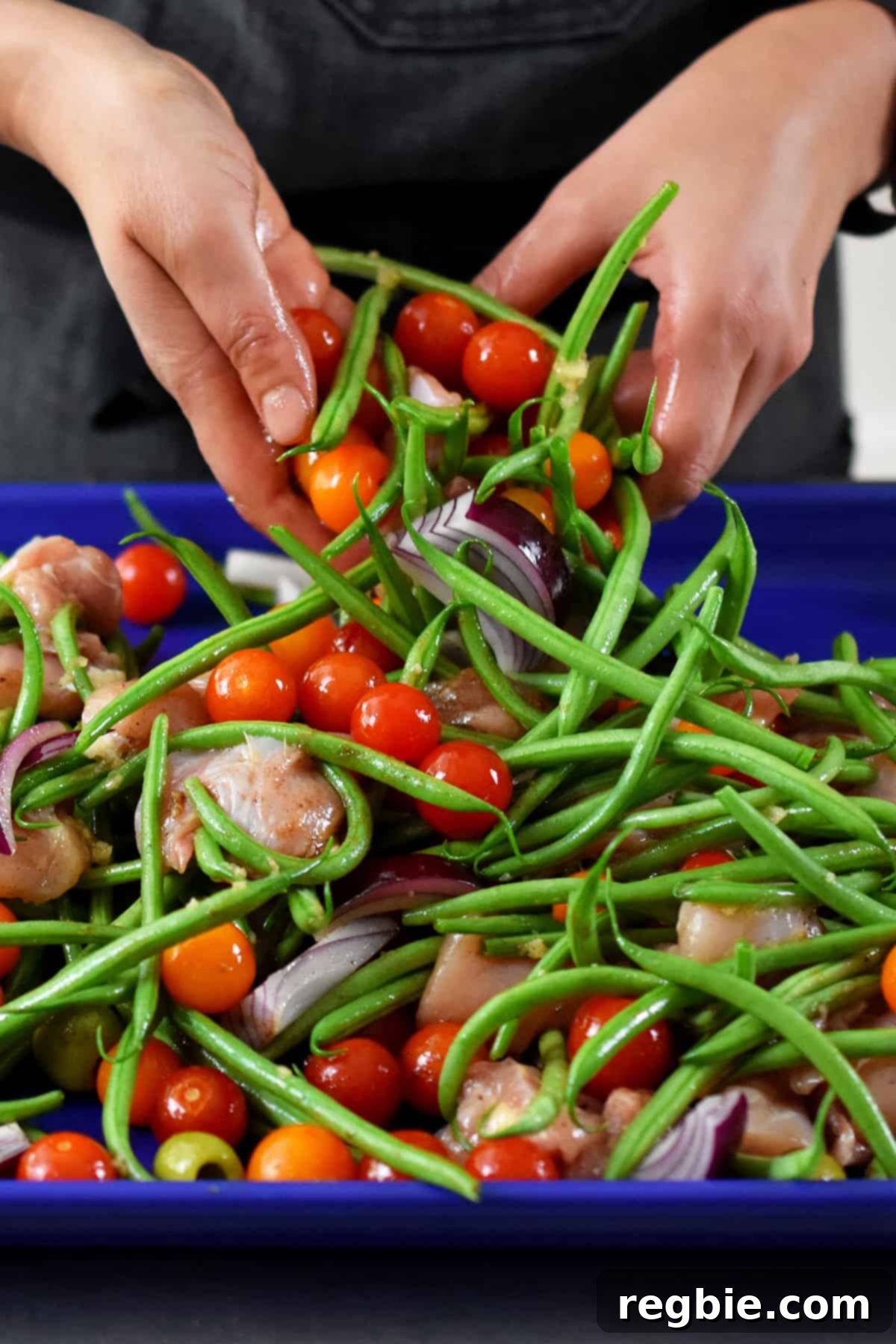 Close-up of hands tossing the ingredients for sheet pan Italian chicken, ensuring they are evenly coated with seasoning and olive oil before spreading them out.