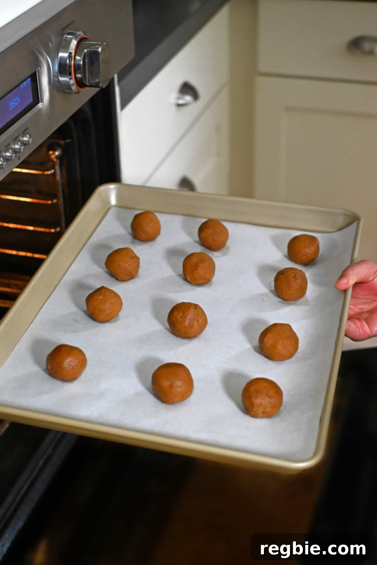 Paleo Pumpkin Bliss Cookies 17 A parchment lined rimmed baking sheet is topped with twelve paleo pumpkin cookie dough balls is being placed into an open oven.