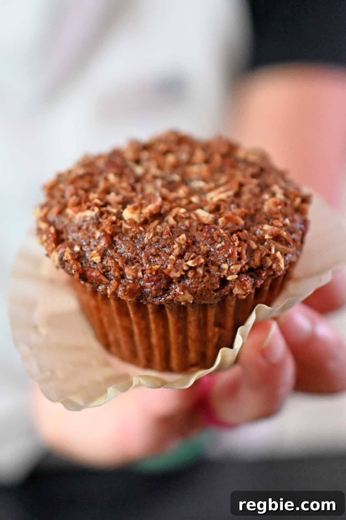 A hand holding a paleo and gluten free apple muffin with the paper liner unwrapped, showcasing its tender crumb and streusel topping.