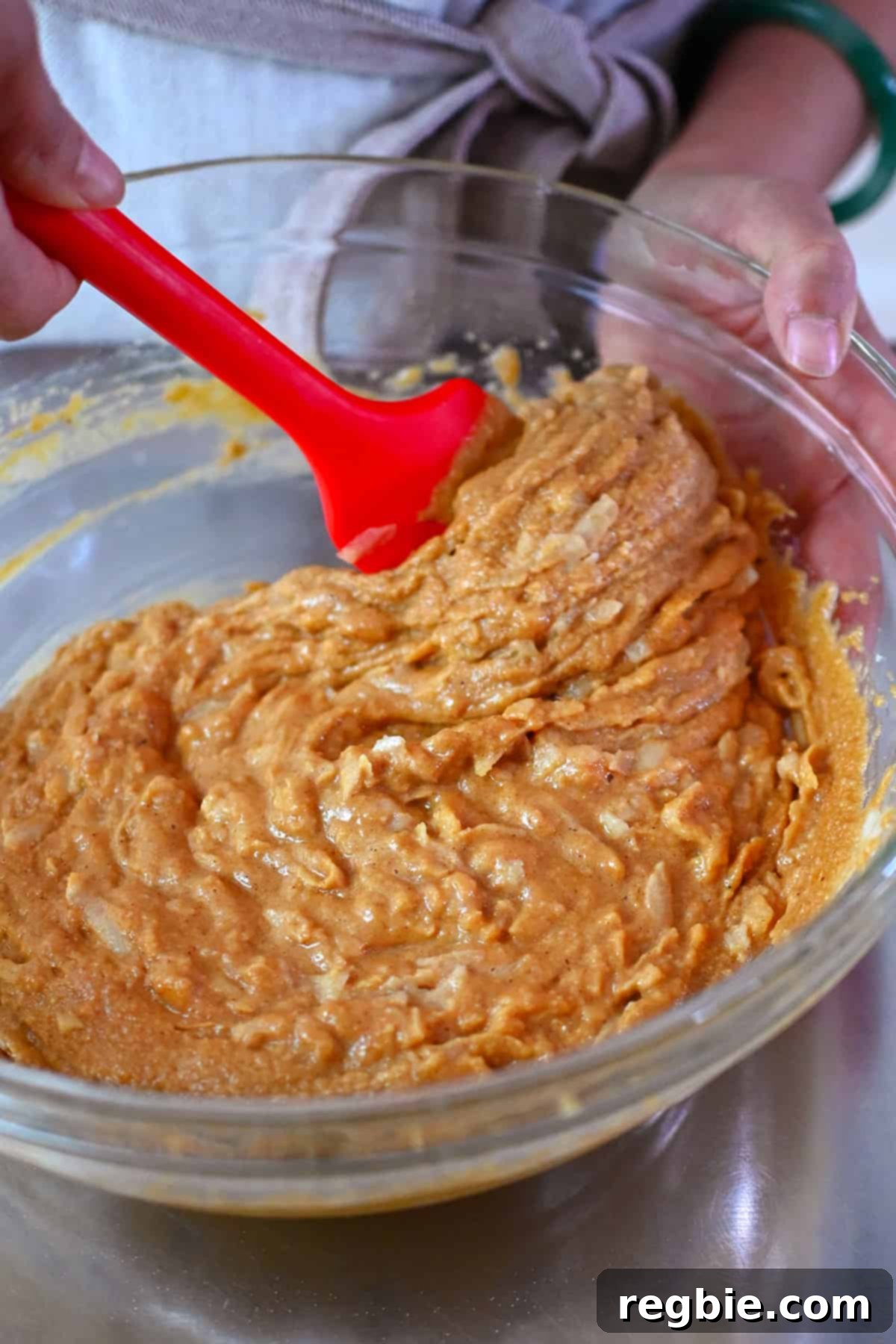 A closeup of the raw paleo apple muffin batter in a large mixing bowl being mixed with a red spatula, showing the shredded apple incorporated.