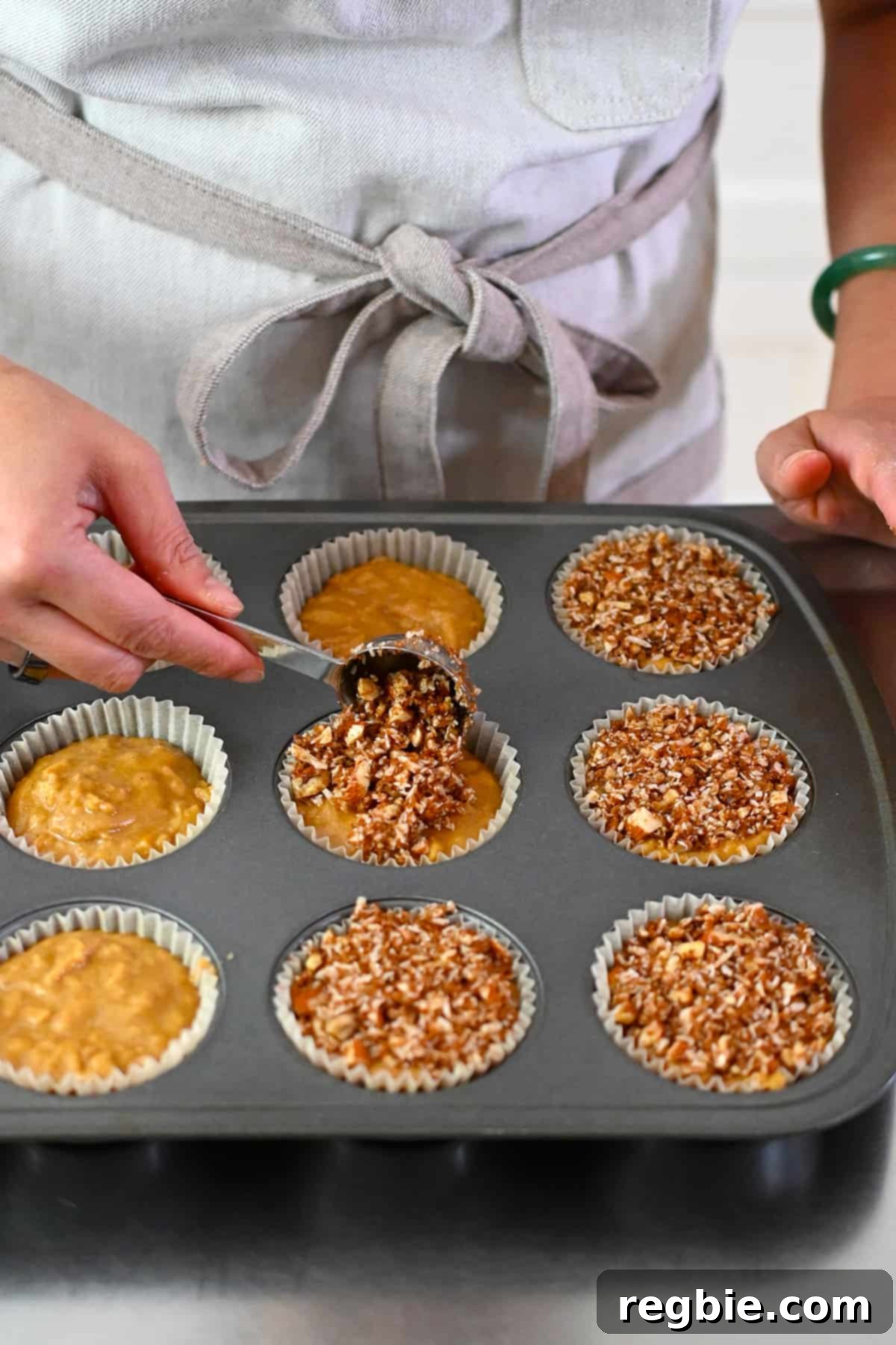 Adding a spoonful of grain-free streusel on top of paleo muffins ready to be baked.