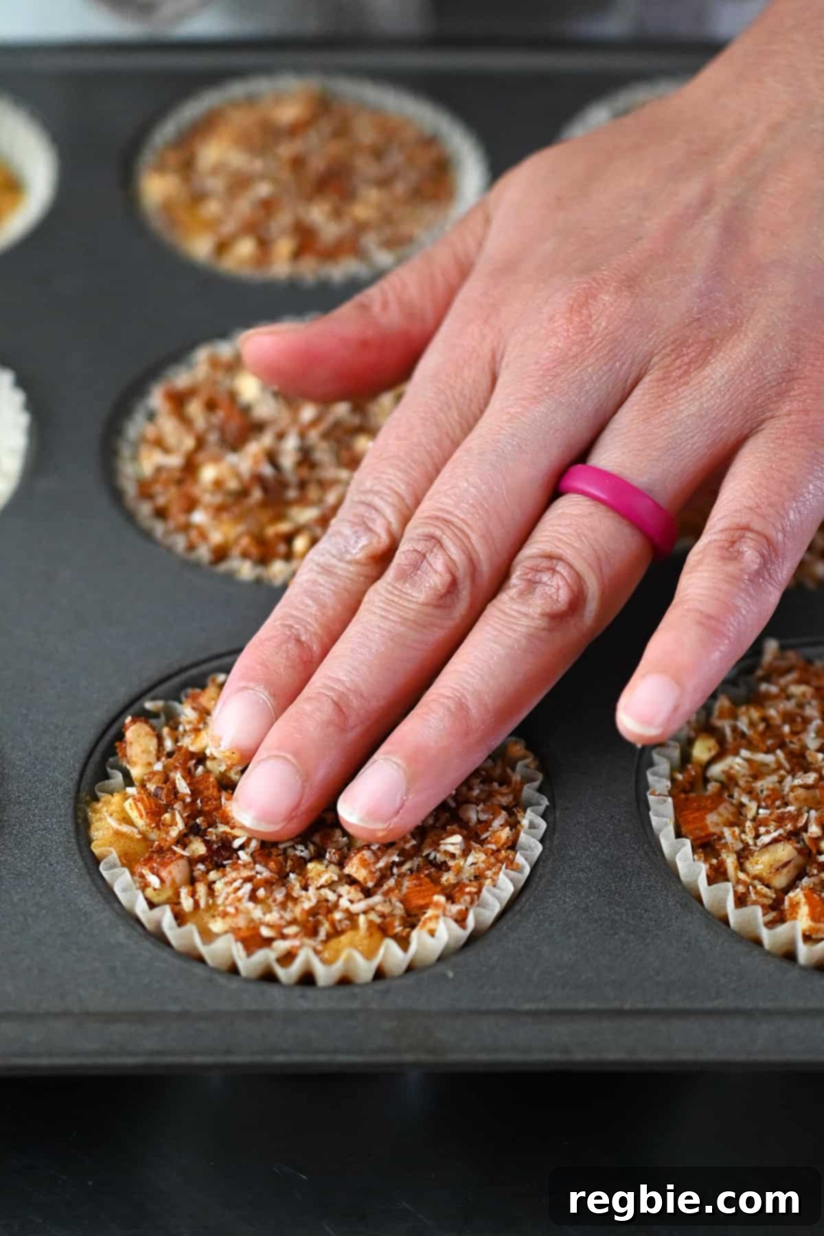 A closeup of fingers pressing down paleo streusel topping on the top of raw apple muffin batter in a muffin pan.