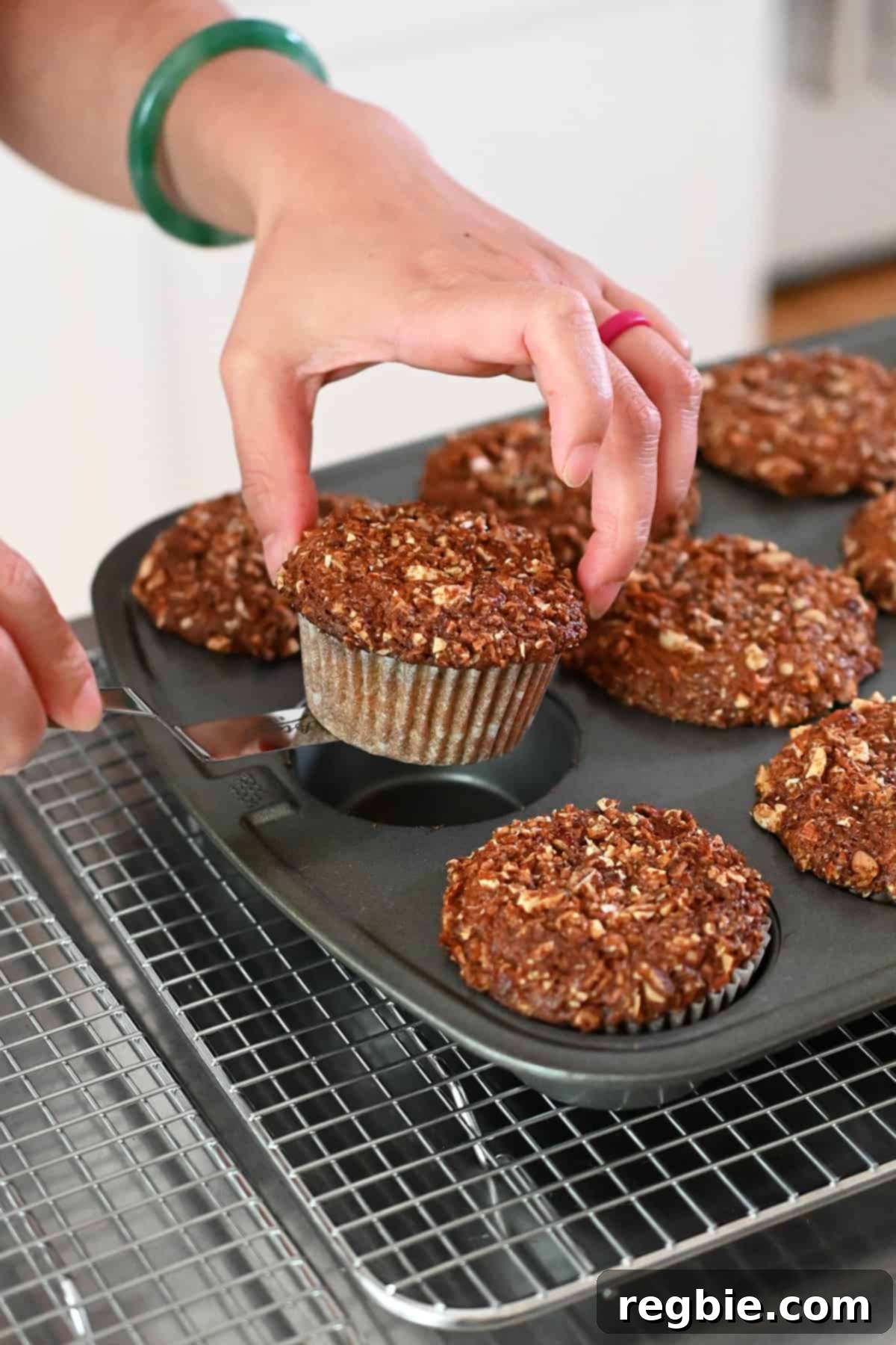 Removing the baked apple muffins from the muffin pan with a small offset spatula and transferring them to a wire cooling rack.