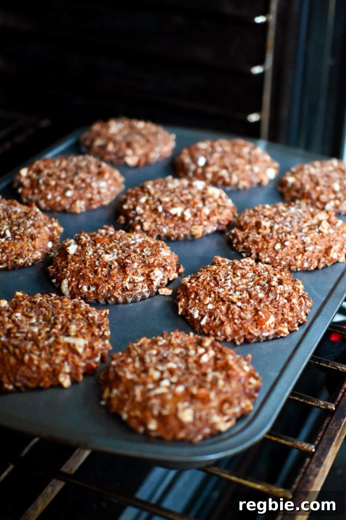 An open oven with freshly baked paleo apple muffins ready to be taken out, showing their golden-brown tops.