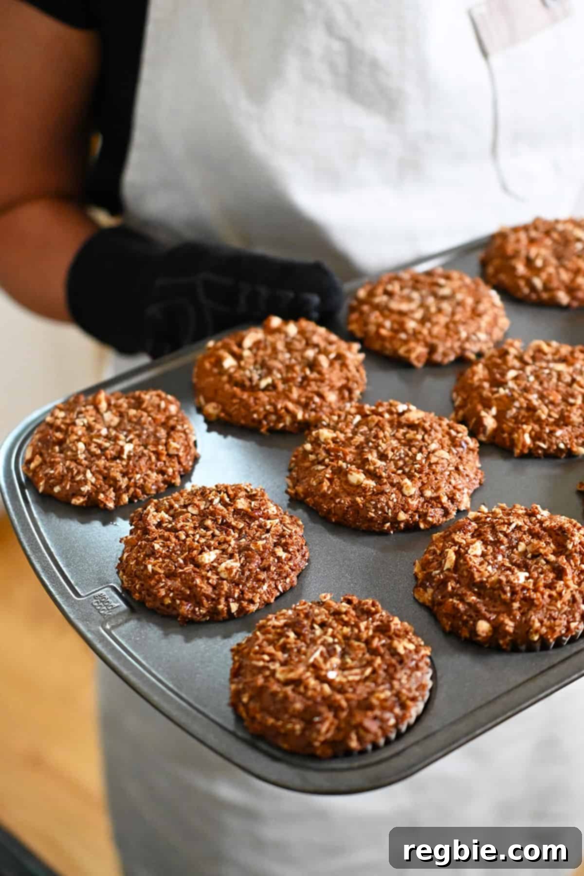 A side view of someone holding a hot pan of apple muffins fresh from the oven, showing their golden tops.
