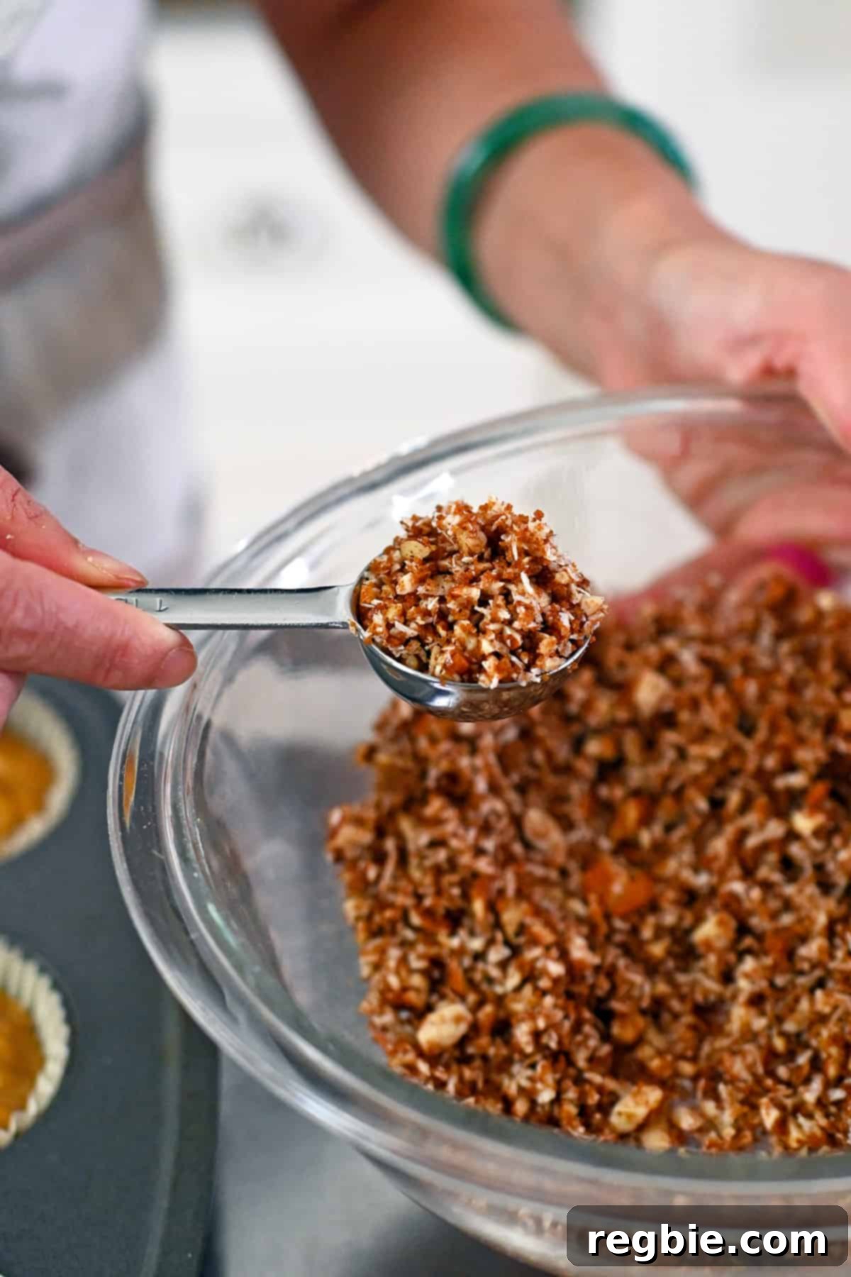 A tablespoon is used to scoop up the paleo streusel topping for the apple muffins, showing its crumbly texture.