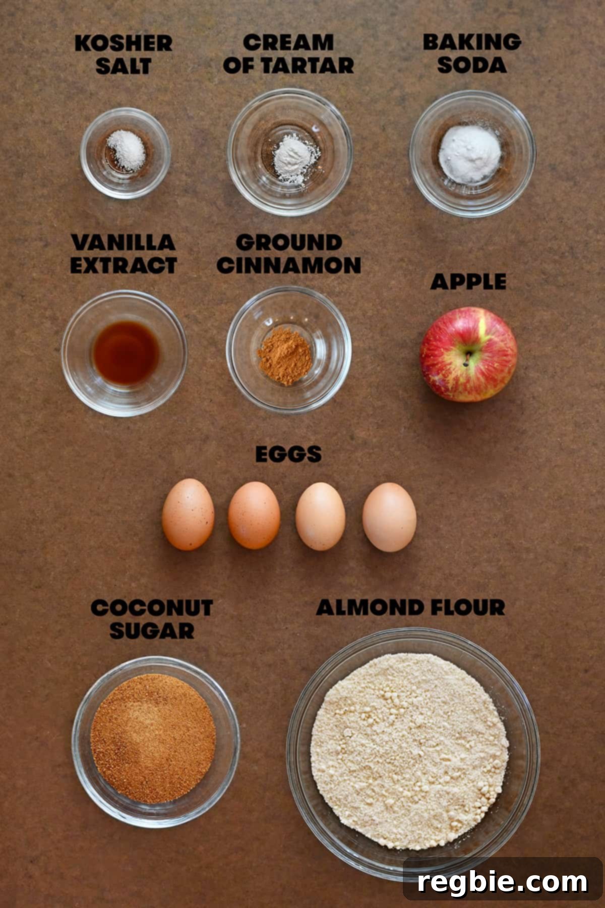 Raw ingredients for apple muffins are measured out in bowls, including almond flour, eggs, and shredded apple.