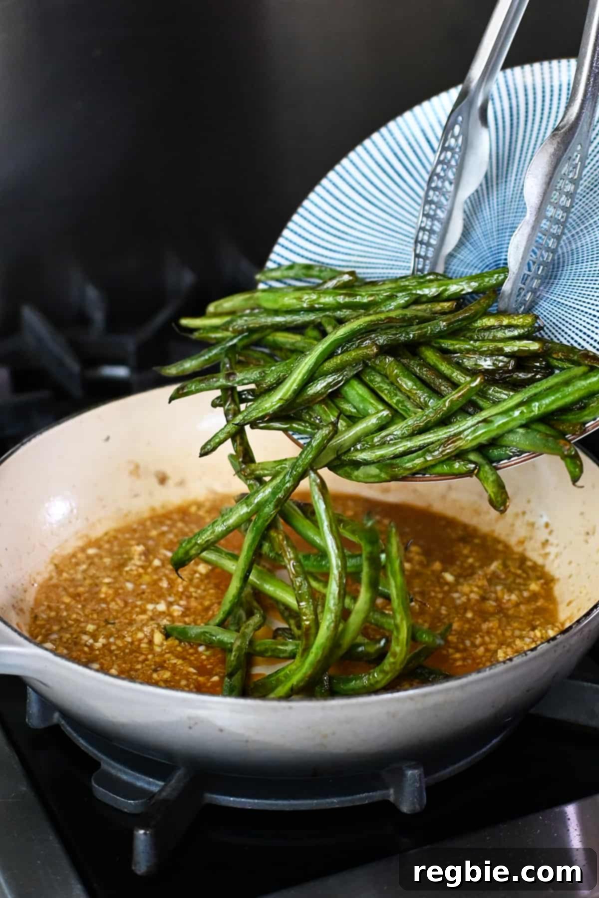Adding the previously blistered green beans back into the skillet, now filled with the aromatic garlic sauce.