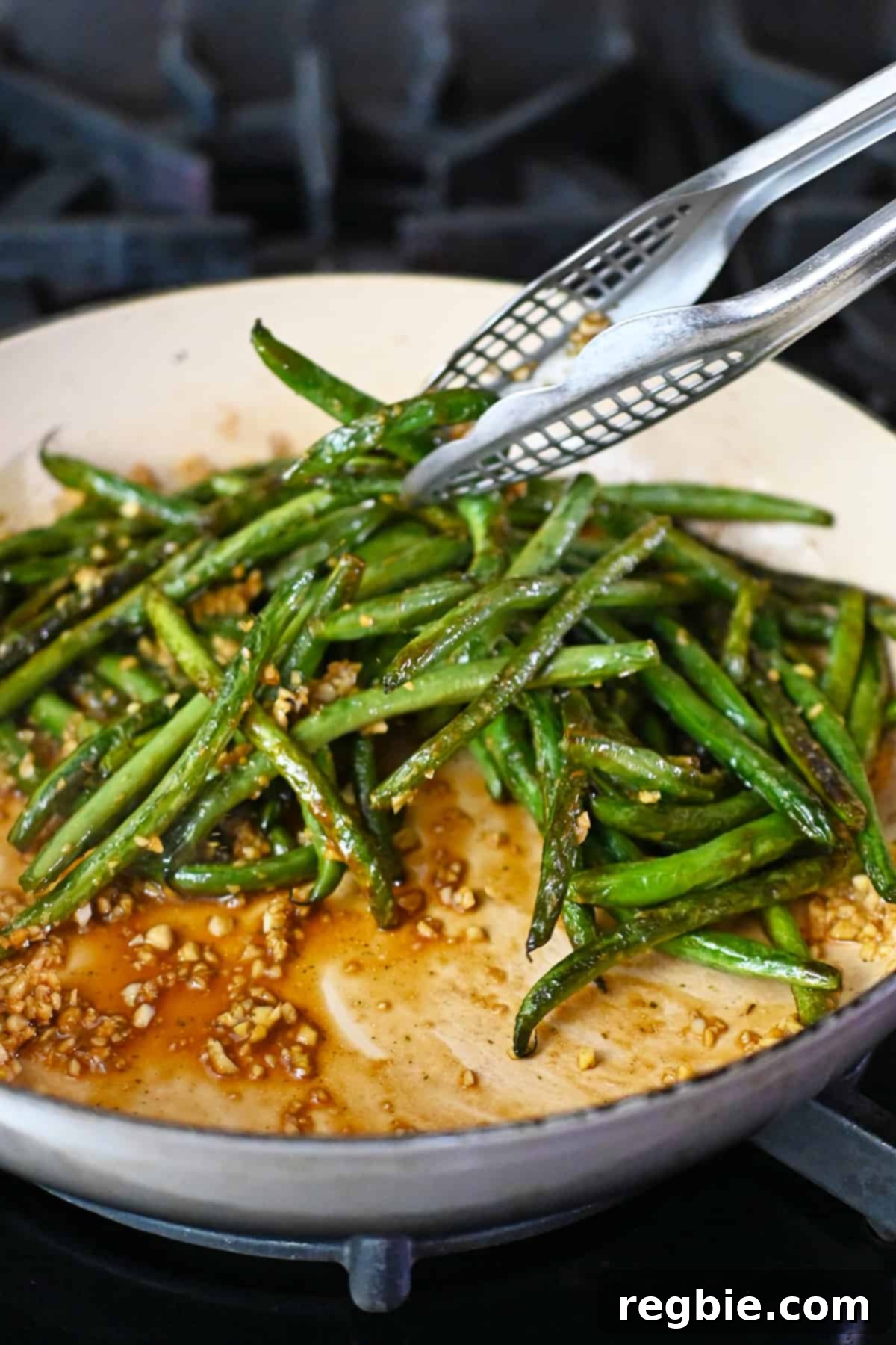 Tossing the blistered green beans vigorously in the pan to ensure they are fully coated with the delicious Chinese garlic sauce.
