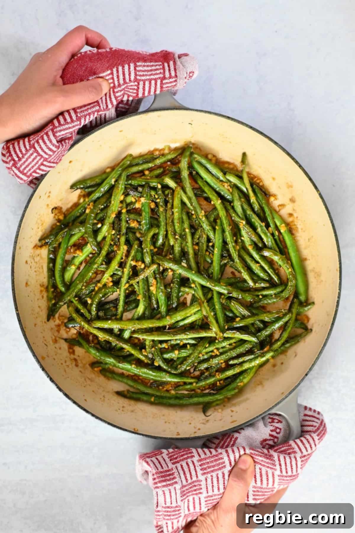 An overhead shot of an enameled cast iron skillet filled with glossy, perfectly cooked Chinese garlic green beans.