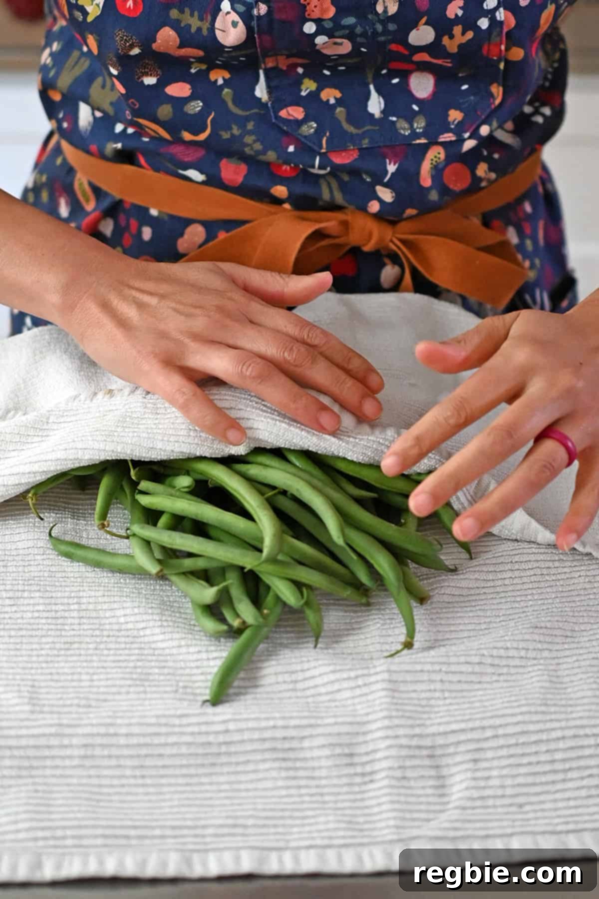 A person patting washed raw green beans dry with a clean kitchen towel, a crucial step before stir-frying.