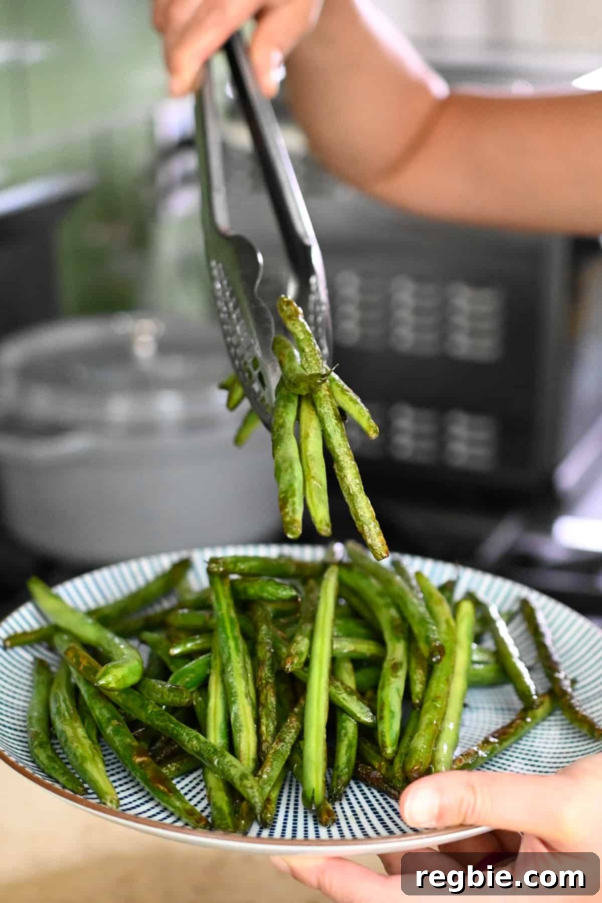 Transferring perfectly cooked, blistered green beans onto a blue and white platter.