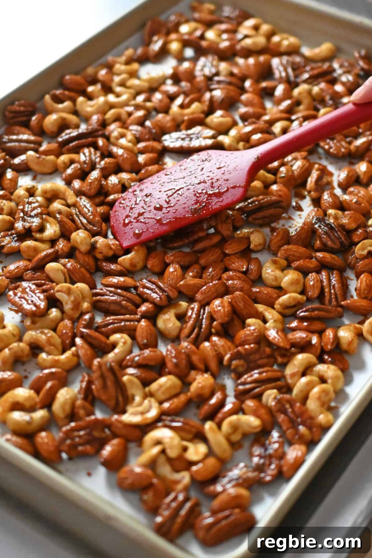 A silicone spatula meticulously arranging the seasoned nuts in a single, even layer on a parchment-lined, rimmed baking sheet, ready for the oven.