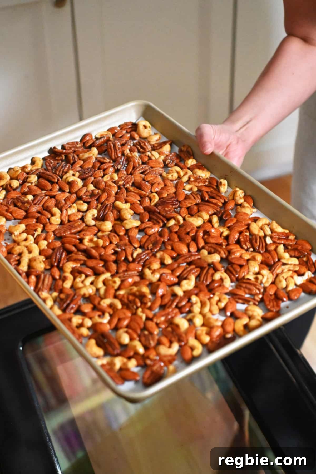 A tray of raw spiced nuts being gently placed into an open oven, beginning their transformation into a golden, fragrant snack.