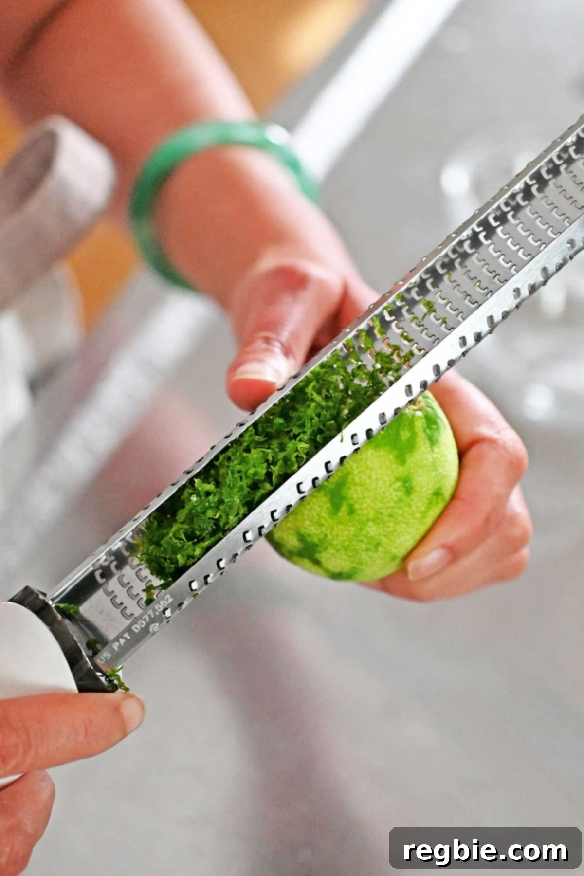 A hand expertly zesting a vibrant green lime using a microplane grater, capturing fine, aromatic zest.
