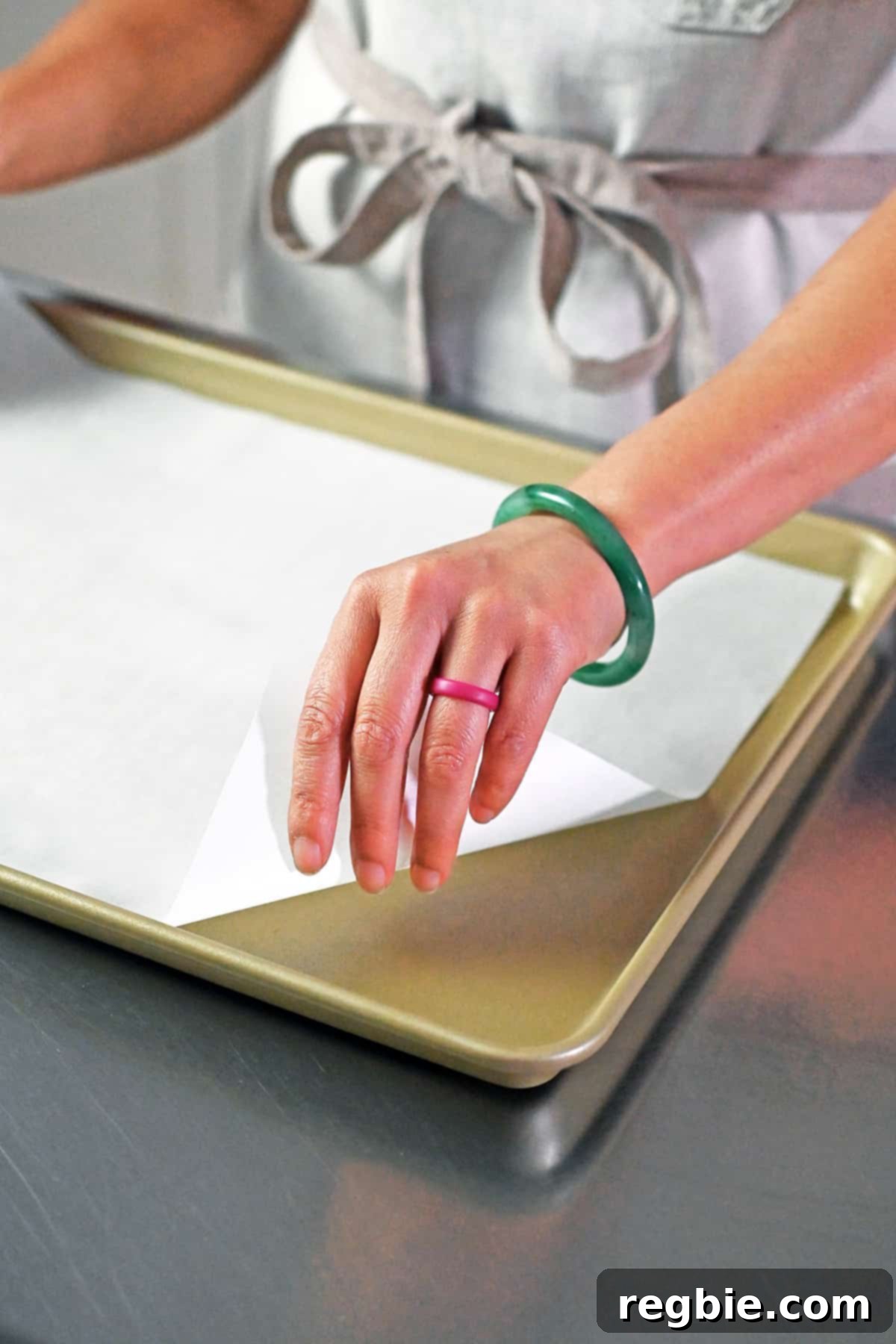 A hand gently placing a sheet of parchment paper into a rimmed baking sheet, preparing it for the nuts.