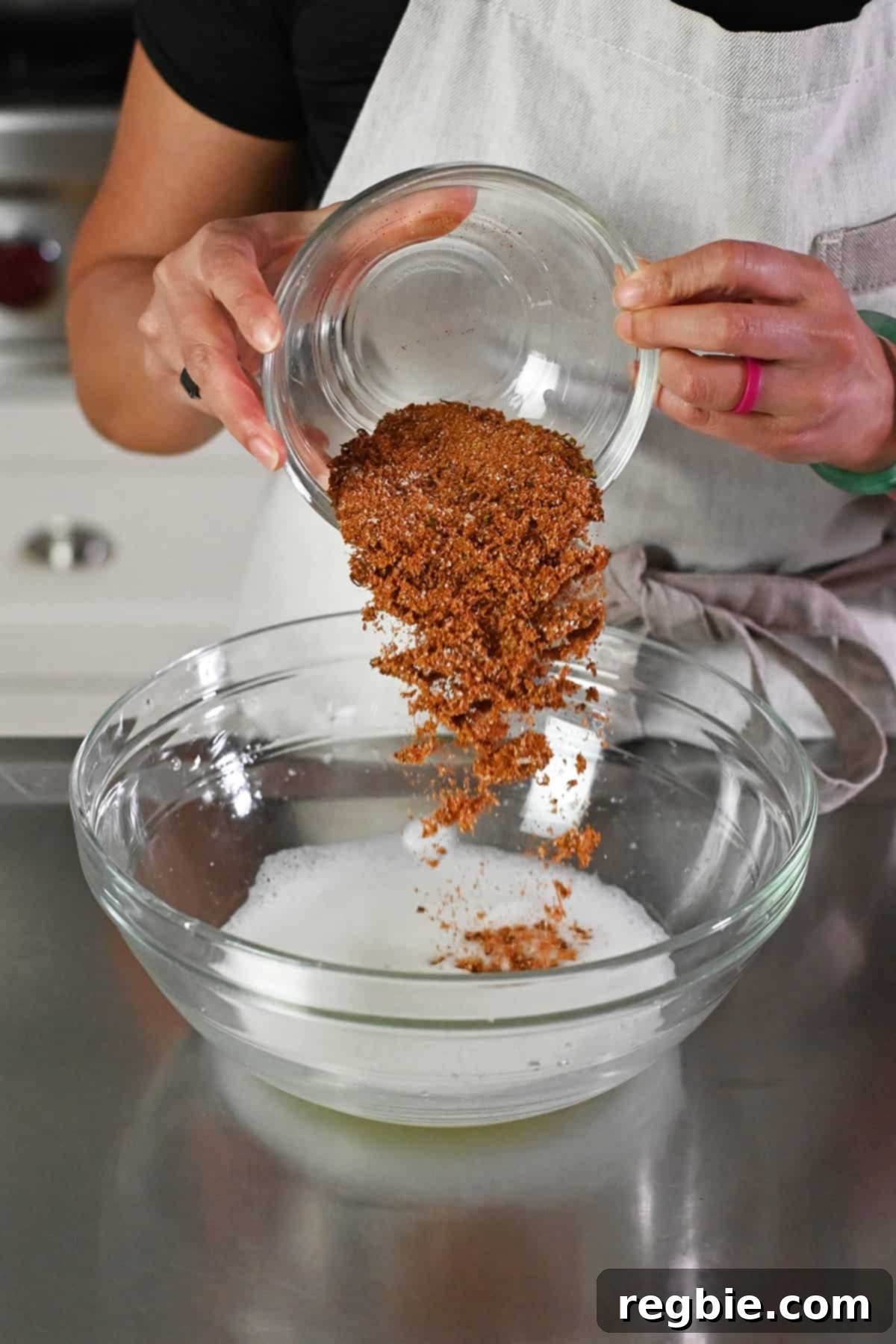 A close-up image showing the act of pouring the vibrant spice blend into a large bowl already containing frothy, whipped egg whites.