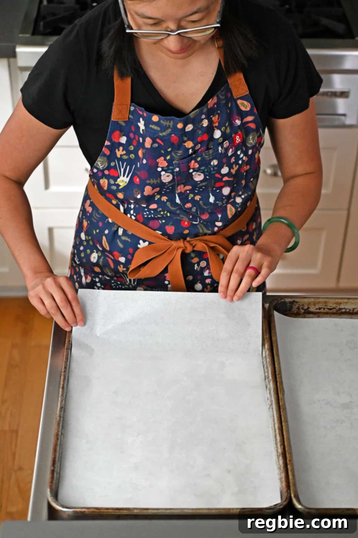 Lining two rimmed baking pans with parchment paper, preparing them for the cookie dough.