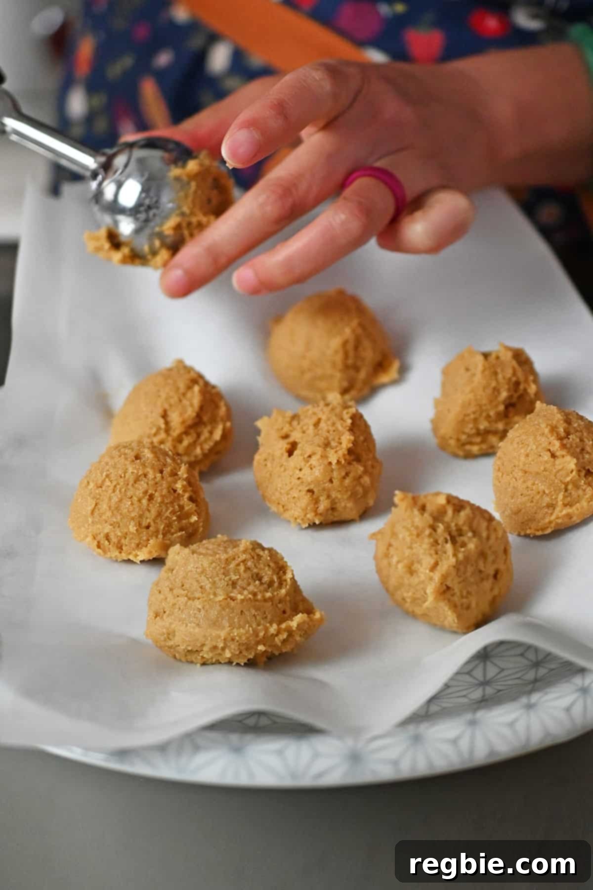 Raw snickerdoodle cookie dough balls being portioned out with an ice cream scoop onto a parchment-lined plate.