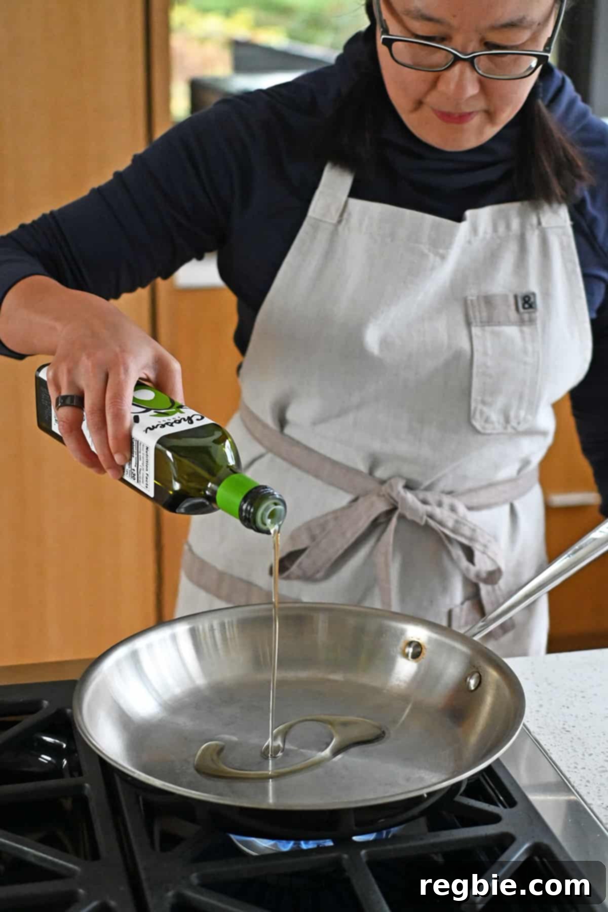 An Asian woman adds avocado oil into a hot large stainless steel skillet.