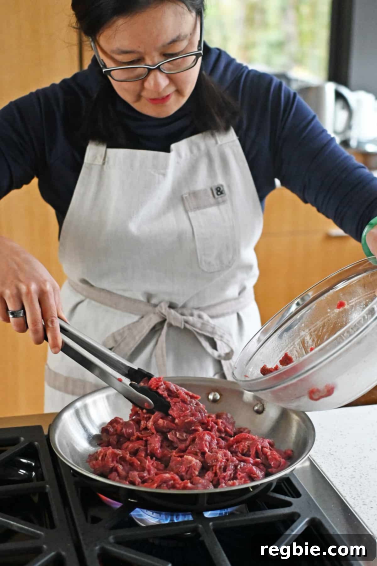 An Asian woman adds marinated sliced flank steak into a hot skillet to make paleo pepper steak.