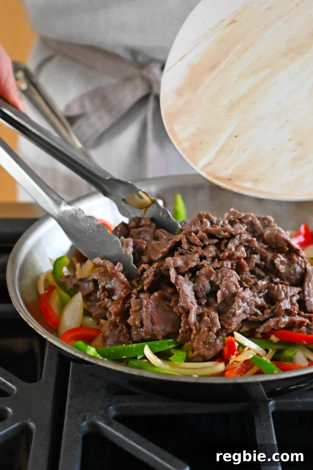 Adding the cooked beef into the pan of sautéed onions and bell peppers.