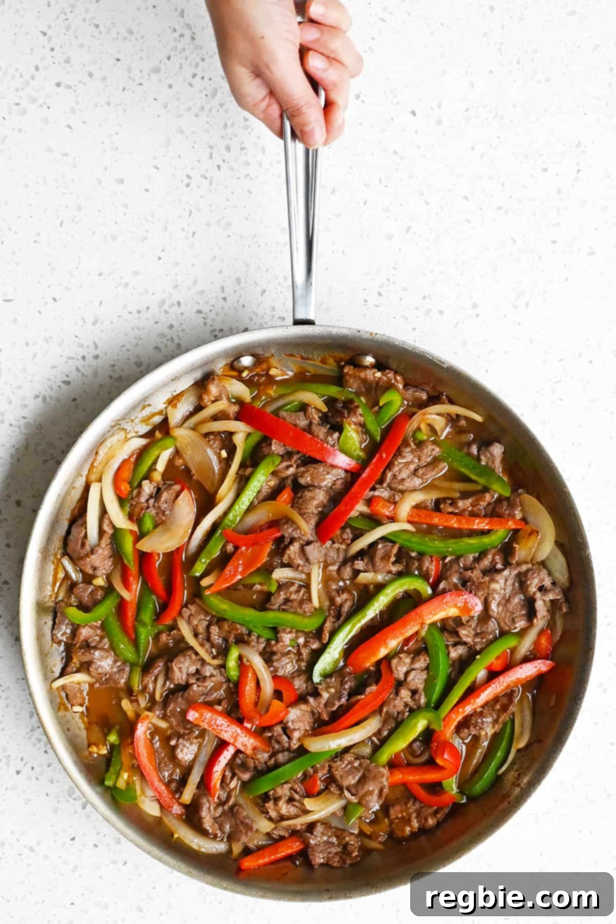 An overhead shot of a hand holding the handle of a skillet filled with paleo and gluten free pepper steak.