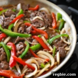 A side view of a skillet filled with cooked paleo and gluten free pepper steak.