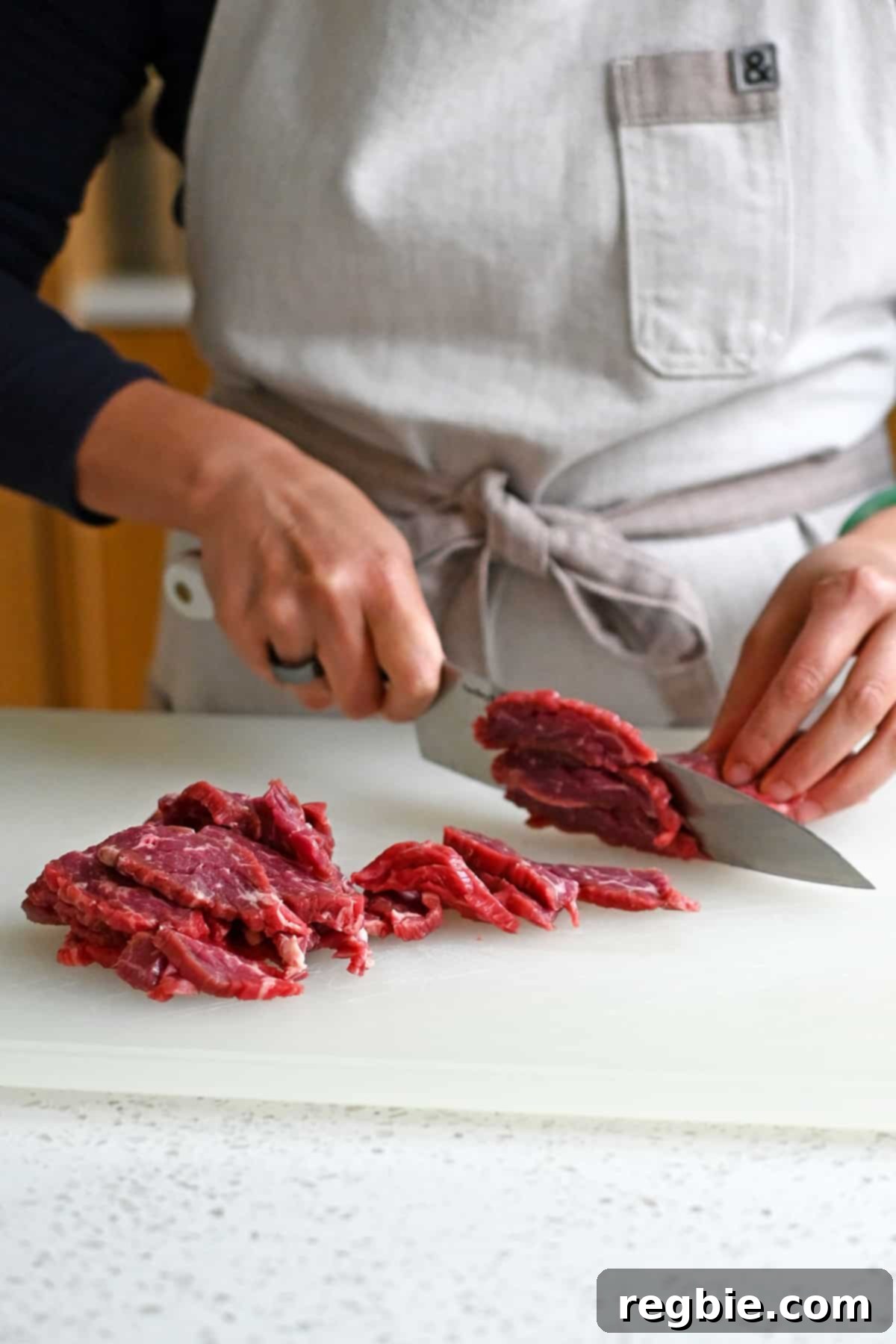Slicing raw flank steak into thin strips against the grain with a chef's knife.