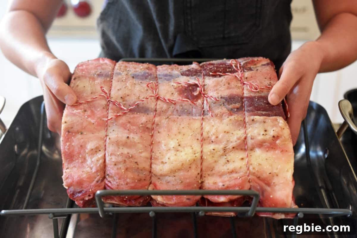 A seasoned prime rib roast being carefully placed onto a roasting rack inside a roasting pan, ready for the oven.