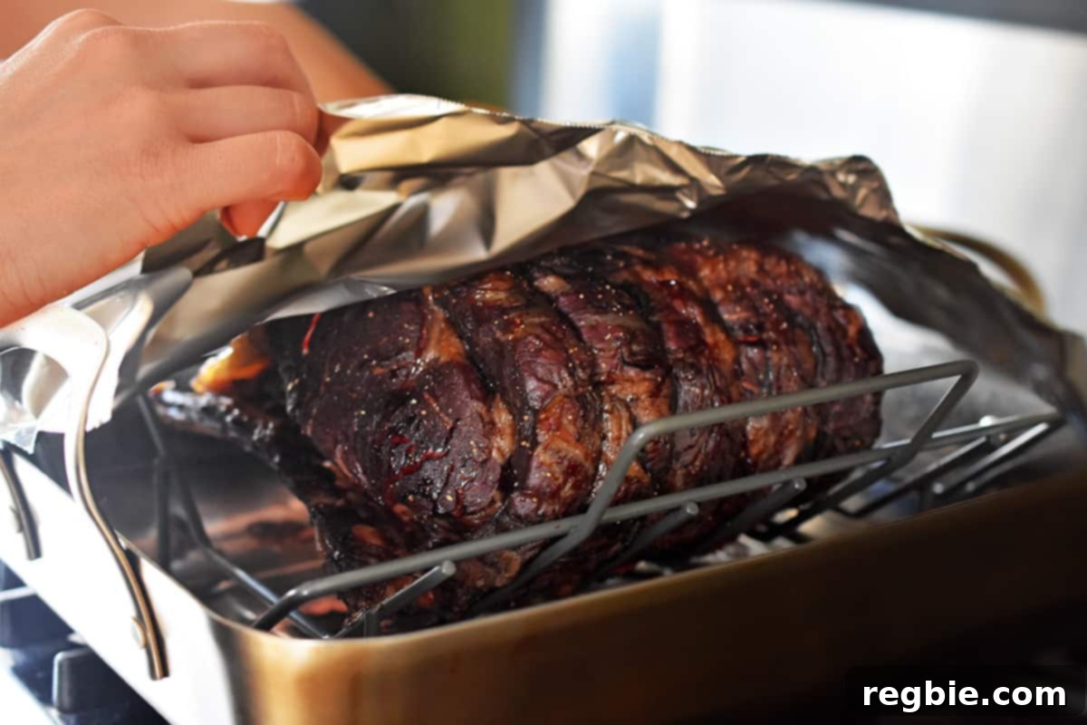 Tenting a perfectly cooked prime rib roast with foil in a roasting pan to allow it to rest and retain warmth.