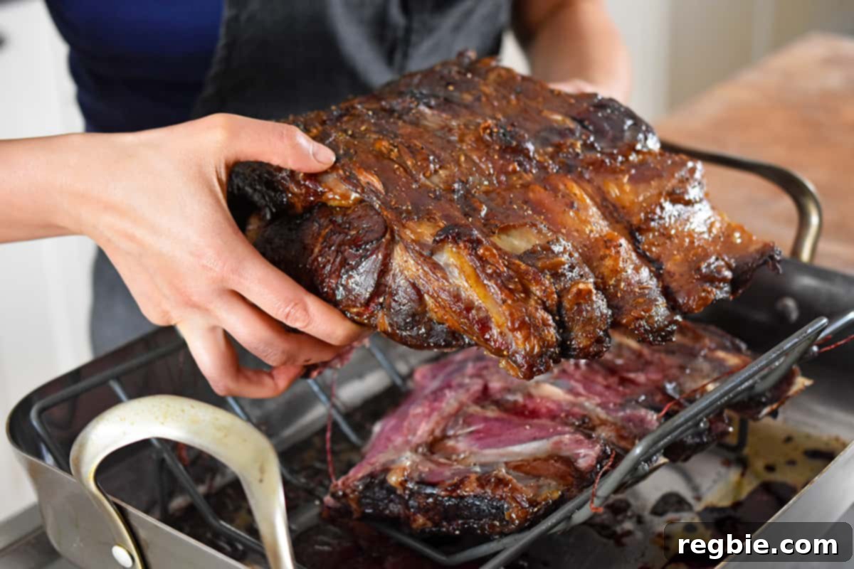 Two hands carefully removing a cooked boneless prime rib roast from a roasting pan, ready for carving.