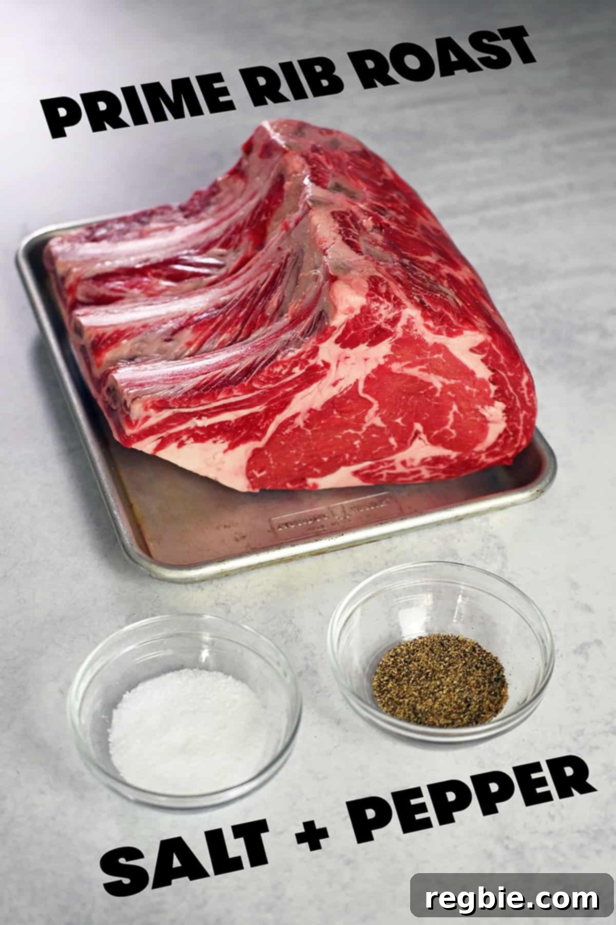The raw ingredients laid out to make a prime rib roast: a large beef rib roast, a bowl of kosher salt, and a pepper mill.