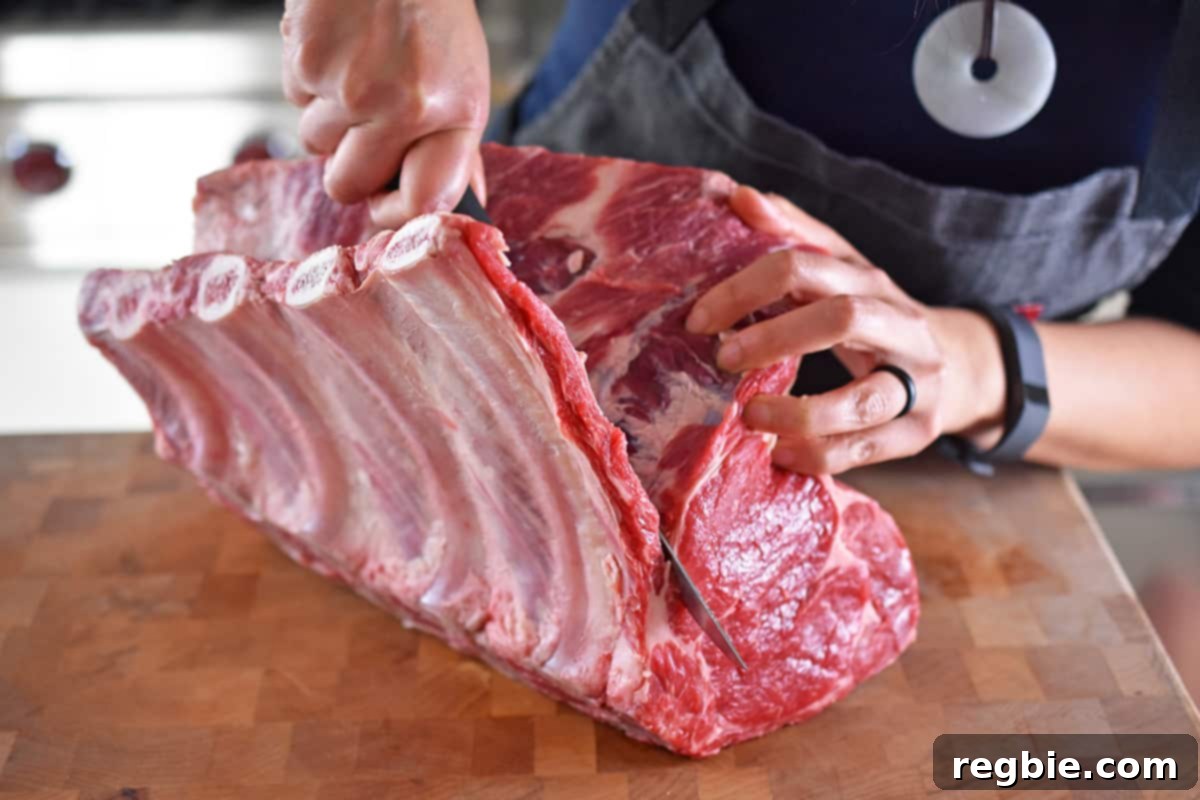 Someone using a boning knife to expertly remove the bones from a raw prime rib roast on a cutting board.