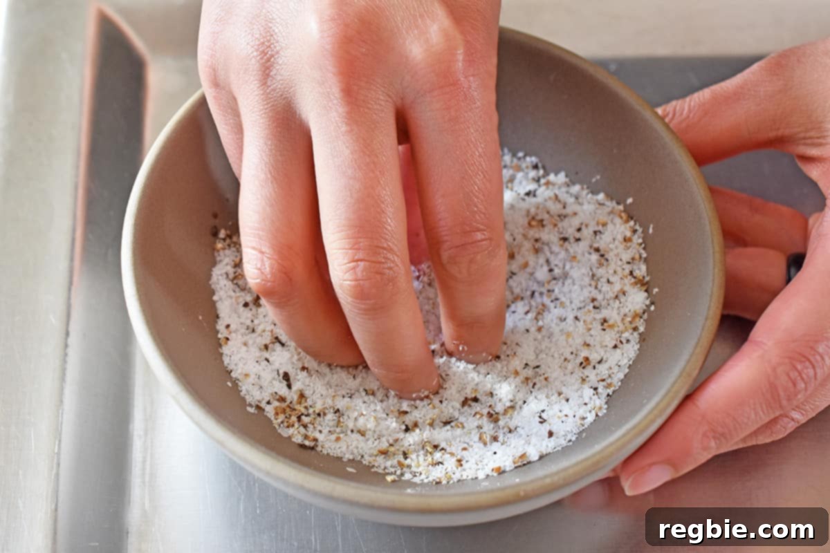 A hand is mixing a generous amount of salt and pepper in a small bowl, preparing the rub for the prime rib roast.