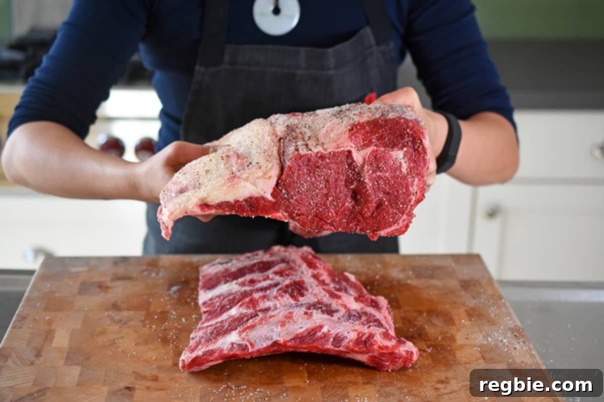 Someone meticulously tying a seasoned, boneless prime rib roast onto its detached bone rack using butcher's twine, with the fat cap facing up.