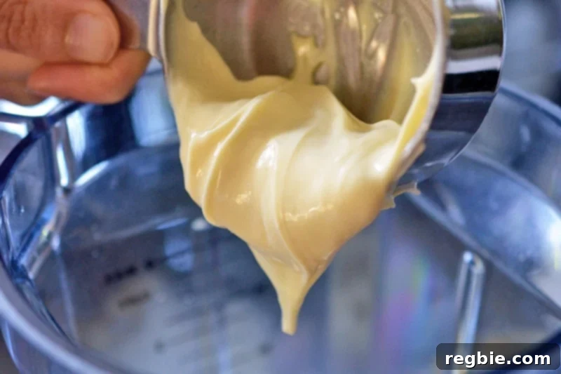 A hand is adding paleo mayonnaise to an open blender container, contributing to the rich creaminess of the Tonnato Sauce.