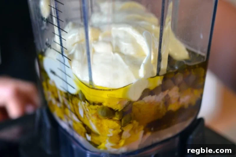 A side shot of a blender filled with all of the Tonnato Sauce ingredients before it is turned on, poised for transformation.