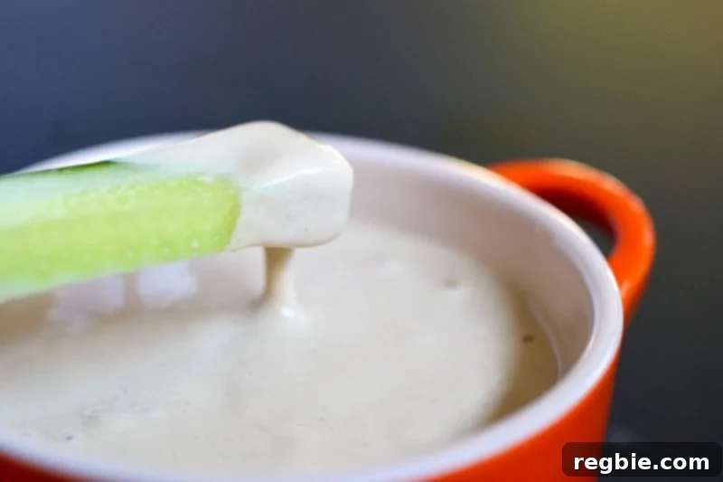 A slice of crisp cucumber being dipped into a bowl of creamy Tonnato Sauce, showcasing a delightful appetizer.