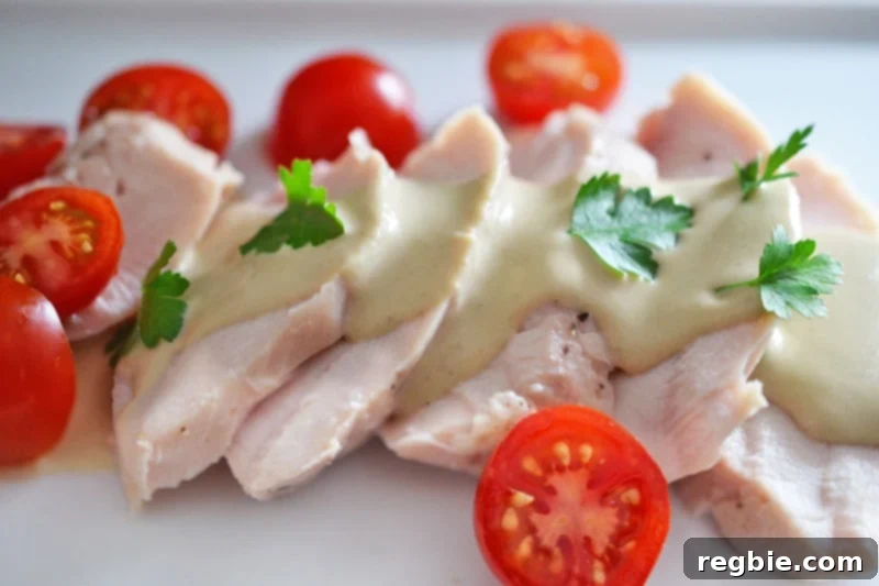 A white plate topped with tender poached chicken and vibrant sliced cherry tomatoes, elegantly drizzled with homemade Tonnato Sauce.