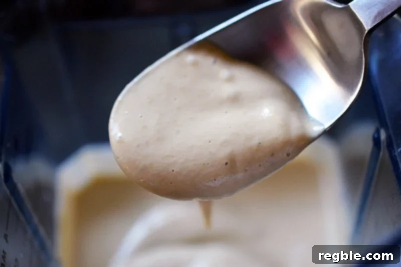 A spoon filled with a thick, beige colored sauce from a blender, illustrating the creamy texture of Keto Tonnato Sauce.