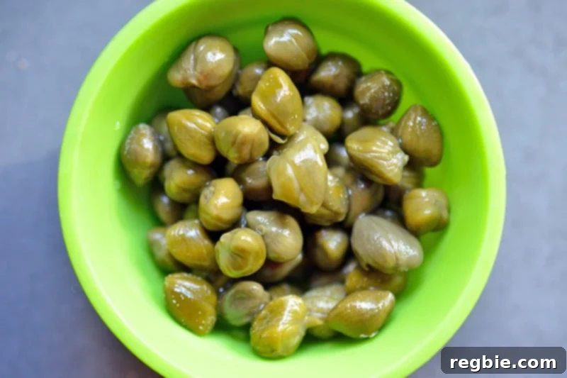An overhead shot of perfectly drained capers in a vibrant green silicone prep bowl, ready to be added to the blender.