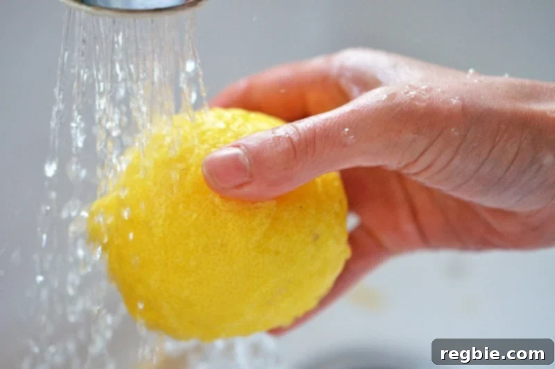 A shot of someone washing a fresh, vibrant lemon under a kitchen faucet, preparing it for the recipe.